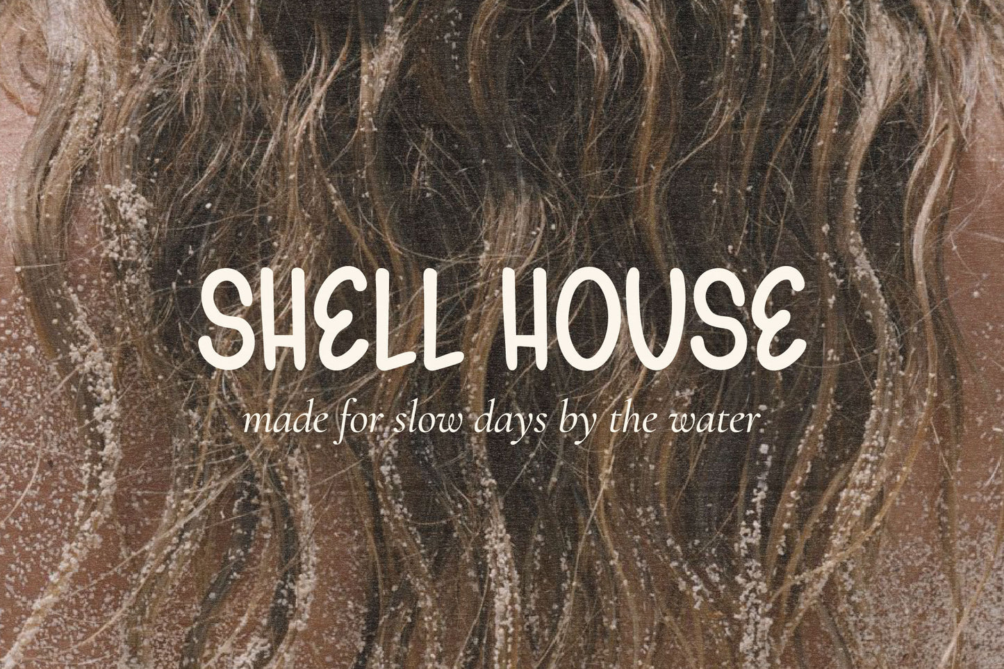 Shell House beachwear logo created with Gelato Daydreams hand-drawn display font over a sandy ocean photograph for relaxed coastal branding and apparel design.