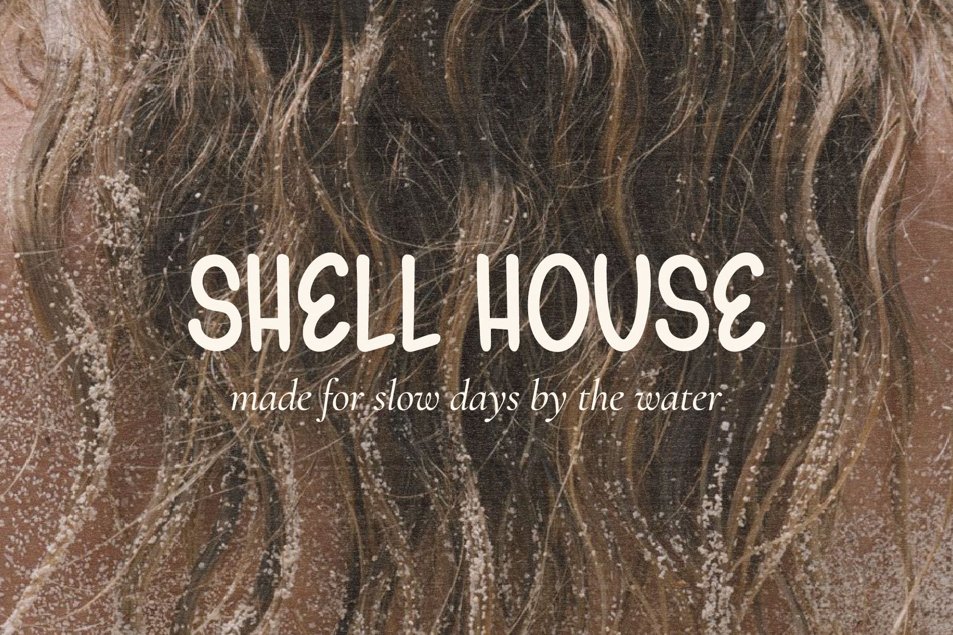 Shell House beachwear logo created with Gelato Daydreams hand-drawn display font over a sandy ocean photograph for relaxed coastal branding and apparel design.